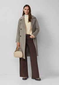 Grau Wollmantel mit schwarzen Knöpfen, cremefarbenem Zopfmuster-Pullover, braunen Schlaghosen und beiger Handtasche. Enthält klobige schwarze Stiefel mit strukturierten Sohlen.