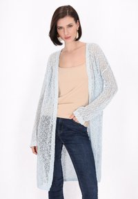 Cardigan azzurro chiaro in maglia con collo aperto, maniche lunghe e vestibilità ampia, abbinato a una maglietta beige e jeans scuri.