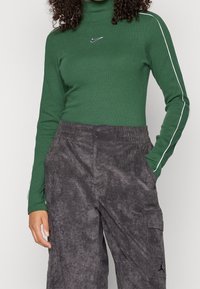 Grön ribbad polotröja med vita sidostråk och Nike-logotyp, i kombination med mörkgrå texturerade cargobyxor med fickor.