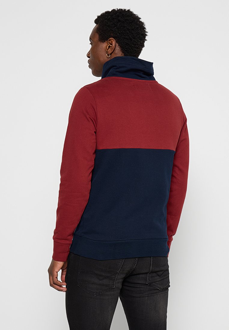 Heren pullover sweatshirt in rood en marineblauw kleurblokken, met een hoge kraag, zachte textuur en geribde manchetten en zoom.