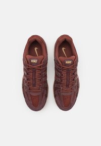 Ett par bruna Nike-sneakers med nät- och mockainformation, snörda skosnören och guldiga Nike-logotyper på tungan och innersulan, visade uppifrån.