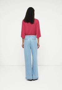 Videbened lys blå denimbukser med høy midje og frynset kant, kombinert med en løstsittende, kortermet burgunder topp.