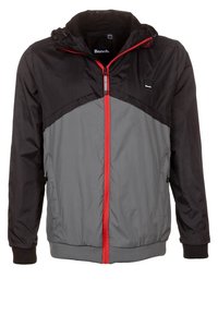 Huvjacka i lättviktstyg. Har en svart övre del, grå nederdel, röd dragkedja och elastiska muddar.