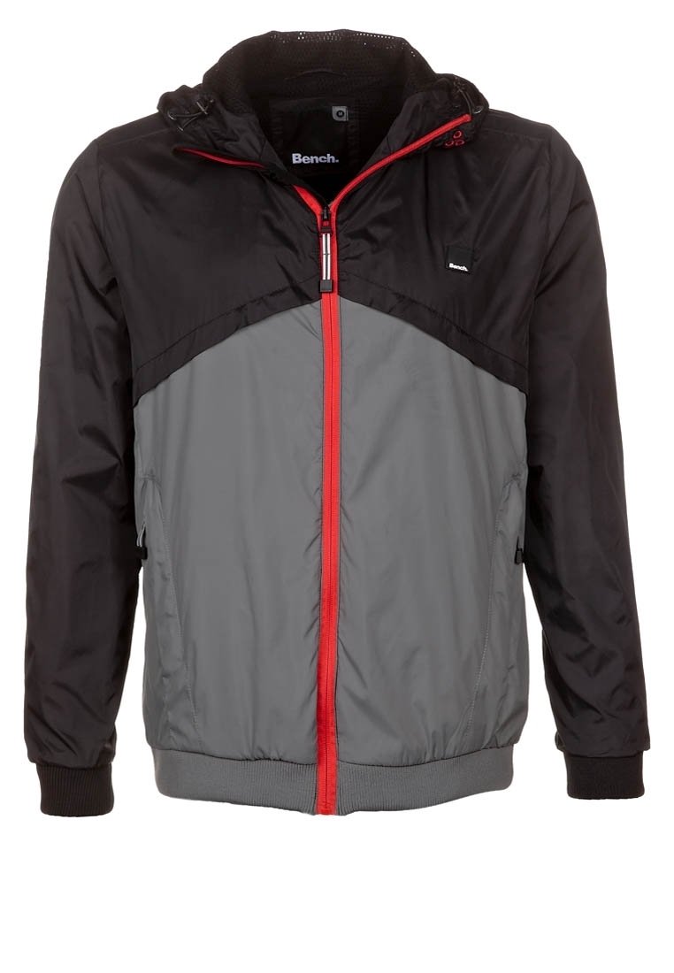 Huvjacka i lättviktstyg. Har en svart övre del, grå nederdel, röd dragkedja och elastiska muddar.