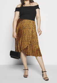 Czarny prążkowany top bez ramiączek, pomarańczowa plisowana spódnica w brązowy leopardski wzór i czarna torebka. Czarny sandały na obcasie dopełniają całość.