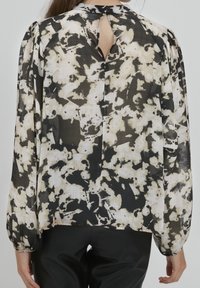 Blusa a maniche lunghe realizzata in tessuto leggero con un motivo astratto nero e beige, dotata di un'apertura a oblò sul retro e maniche arricciate.