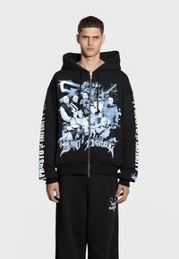 Czarna bluza z kapturem na zamek z graficznym nadrukiem przedstawiającym postaci, z białym tekstem na rękawach i ściągaczami, wykonana z miękkiego materiału bawełnianego.