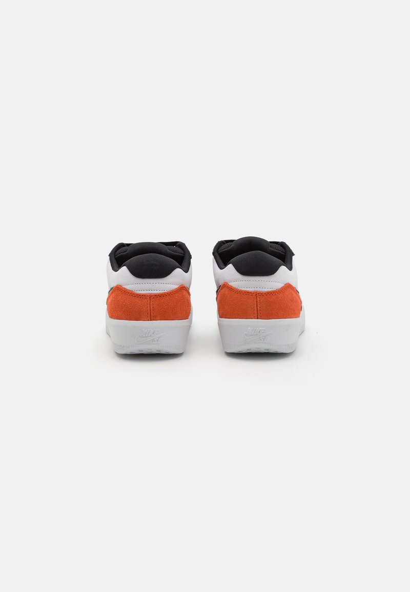Baskets blanches avec des accents en daim orange et un col en textile noir. Semelles en caoutchouc blanches avec un logo sur le talon. Surfaces lisses et forme distincte.
