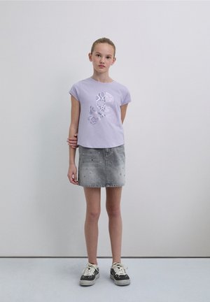 Light purple short-sleeve t-shirt with a graphic design, paired with a gray denim skirt featuring studded accents and black patterned sneakers.