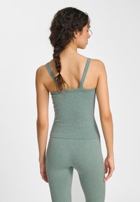 Zielony prążkowany top na cienkich ramiączkach, dopasowany fason i bezszwowe wykończenie. Widok z tyłu ukazuje smukłą sylwetkę i teksturowany materiał.
