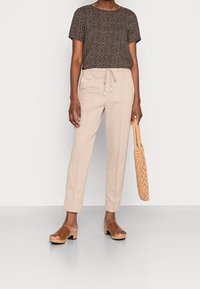 Top negro con pequeño patrón floral blanco, pantalones beige con cuerda, zuecos marrones de punta abierta y bolso tejido color tostado. Tejidos suaves y ligeros.