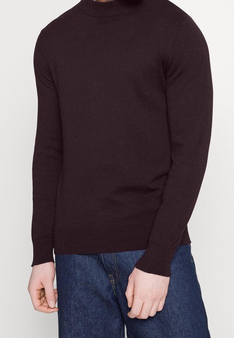 Ciemnobrązowy sweter z długim rękawem, z prążkowanym dekoltem i mankietami, uszyty z miękkiego dzianiny, w połączeniu z niebieskimi dżinsami.