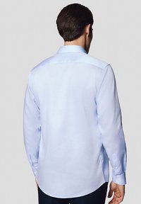 Jasnoniebieska koszula z długim rękawem o gładkiej fakturze, z guzikami na mankietach, spiczastym kołnierzykiem i prostym dołem, widziana z tyłu.