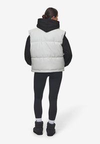 Lysegrå polstret vest med høy krage, kombinert med en svart hettegenser, svarte leggings og svarte støvler. Nøytral fargepalett.