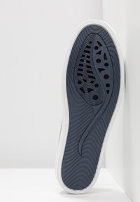 Semelle de chaussure en bleu marine avec des bordures blanches, présentant des rainures décoratives, des évents d'air et des accents de design botanique. Taille 37 inscrite sur le côté.