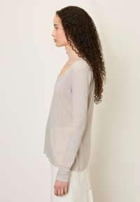 Svetlošedý dlhý rukáv s výstrihom do V, mäkkou textúrou a voľným strihom, kombinovaný s bielou sukňou. Výrazné detaily bočných švov.