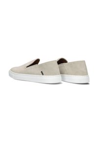 Beige Wildleder Slipper-Sneaker mit weißen Gummisohlen und einem kleinen schwarzen Etikett an der Seite, aus einer Rückansicht in drei Viertel-Ansicht gezeigt.
