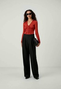 Red long-sleeve top with a button-down front and gathers, paired with high-waisted black wide-leg trousers and a small black handbag.