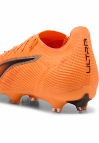 Scarpino da calcio arancione con superficie testurizzata, design elegante, dettagli neri e tacchetti trasparenti per trazione. Presenta il marchio "ULTRA".