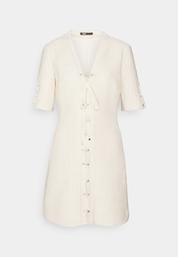 Robe à manches courtes et col en V, fabriquée en tissu crème texturé, avec un laçage frontal à œillets métalliques et des boutons décoratifs sur les manches.