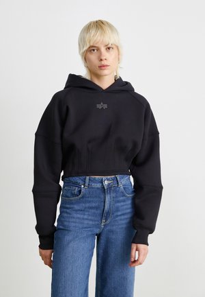 Haut à capuche noir court avec une grande capuche, affichant un logo discret sur la poitrine. Assorti à un jean en denim bleu taille haute.