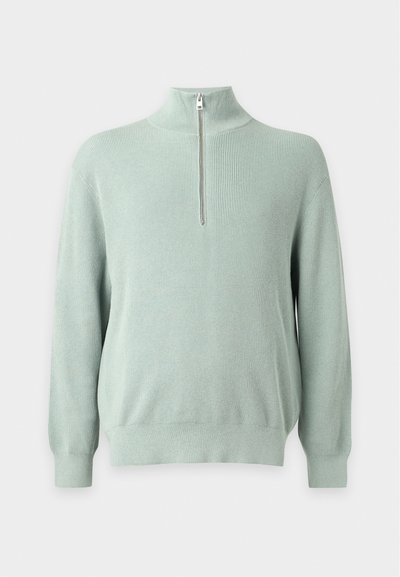 Pull en tricot côtelé vert clair avec manches longues et une courte fermeture éclair devant au col montant sur un fond uni.