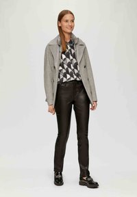 Szary płaszcz z wełny z guzikami podwójnego zapięcia, zestawiony z koszulą w czarno-białą geometryczną grafikę, czarnymi skórzanymi spodniami i czarnymi loafersami.