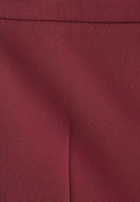Tissu bordeaux avec une texture lisse et un léger éclat, présentant une couture en haut et de subtiles plis. Le textile est léger et flexible.