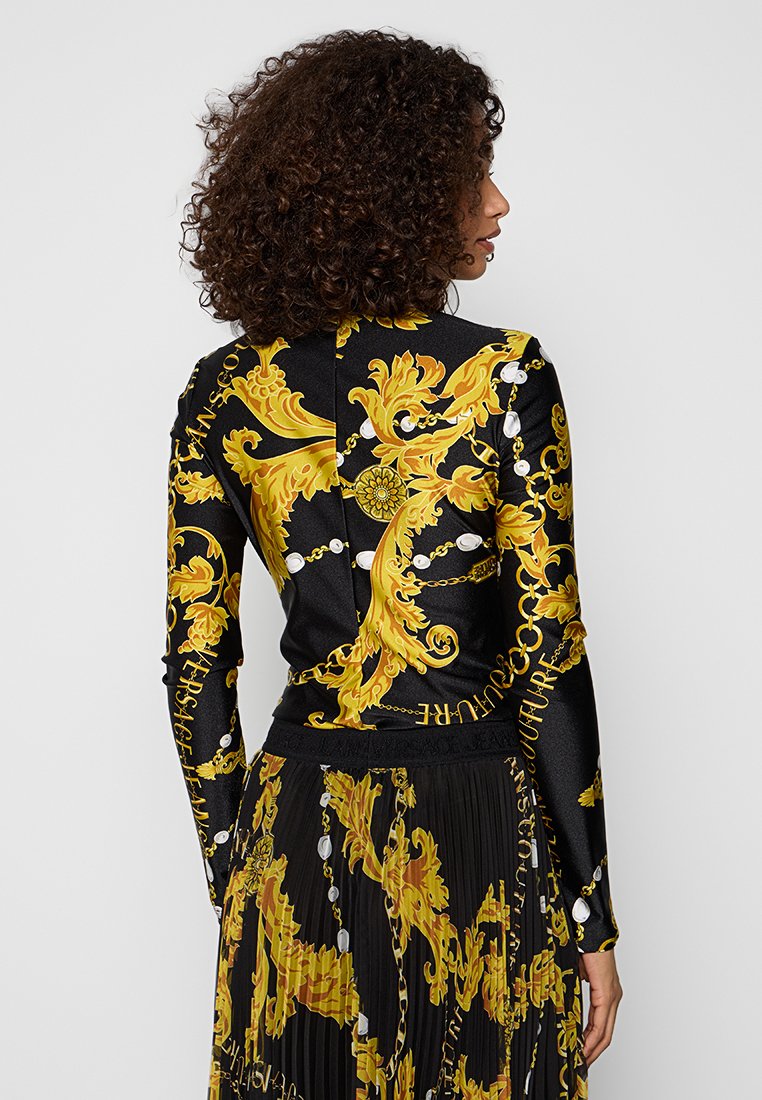 T-shirt à manches longues en satin noir avec des motifs baroques jaunes et des accents de chaîne, présentant une silhouette ajustée et un col rond.