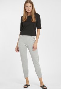 Haut noir à manches courtes associé à un pantalon gris clair, fuselé, avec des poches zippées ; modèle portant des sandales noires à glissière.