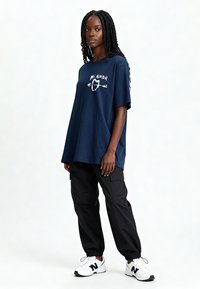 T-shirt en coton bleu marine à coupe oversize, avec un texte graphique blanc "Mi Amor" et un motif de cœur. Associé à un pantalon cargo noir et des baskets blanches.