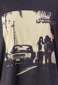 Černé bavlněné tričko s potiskem vintage auta a dvou postav na silnici. Design obsahuje kontrastní krémově zbarvený tisk a texturované detaily.