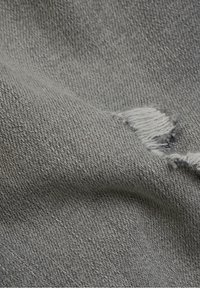 Tela vaquera gris con un área desgastada y bordes deshilachados. La textura es suave con un ligero estiramiento y un acabado mate.