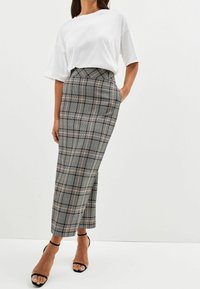 T-shirt bianco oversize abbinato a una gonna a pieghe a vita alta in tartan nei colori nero, grigio e rosa, con silhouette dritta e tasche laterali.