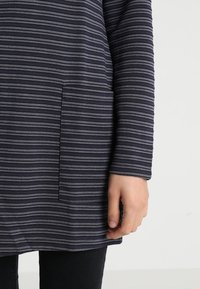 Tunique à manches longues en bleu marine foncé avec des rayures horizontales gris clair. Elle dispose d'une poche à l'avant et d'une coupe décontractée. Tissu doux au toucher.