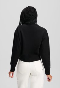 Μαύρο cropped sweatshirt με μακριά μανίκια και ριμπ ύφανση στις μανσέτες, συνδυασμένο με λευκά παντελόνια που διαθέτουν ραμμένη λεπτομέρεια στο πλάι. Μαλακή υφή υφάσματος.