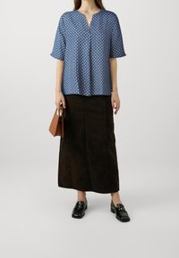 Camicia blu a maniche corte con scollo a V e pois bianchi, abbinata a una lunga gonna di jeans marrone e mocassini neri. Incluso borsa marrone.