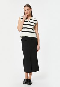 Mouwloze, crèmekleurige en zwarte gestreepte top met een polo-kraag, gecombineerd met een hooggewaaid zwarte rok met twee voorzakken. Zwarte loafers.