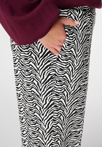 Zebra print broek met zwart-witte strepen, een zachte textuur en een zijzak. De hand van het model zit in de zak.