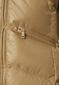 Beżowa pikowana kurtka z ukośną kieszenią na zamek i suwakiem z logo CK.