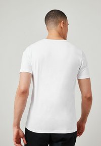 Camiseta blanca de manga corta con cuello redondo, hecha de tela de algodón suave, con un diseño trasero sencillo y liso sin adornos.
