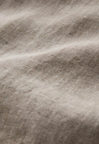 Gros plan sur un tissu beige avec une texture tissée visible et de doux plis créant des ombres subtiles.