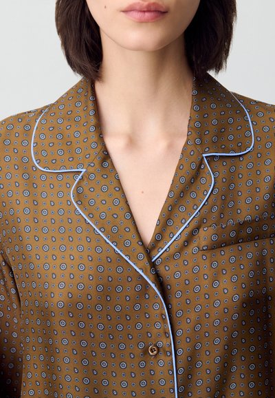 Camicia marrone a fantasia con piccoli disegni circolari blu. Presenta piping azzurro chiaro lungo il colletto e la patta dei bottoni. Taschino sul petto.