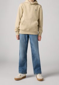 Beige huvtröja med känguruficka, kombinerad med ljusblå, avslappnade denimjeans. Krämfärgade och tan sneakers med gummisulor.