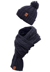 Knitted navy hat with pom-pom and matching scarf featuring a twisted cable pattern. Both items have a leather brand patch.
