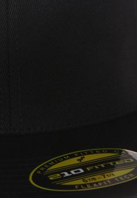 Musta sobiv müts tekstureeritud kangast, lame äärega, millel on kollane silt, mis näitab suurust ja paindlikkuse tehnoloogiat.