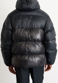Black puffer jacket with a hood, featuring a shiny, quilted design and puffed sections. The material appears lightweight and smooth.