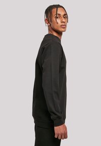 Sudadera nera a maniche lunghe con collo a giro e polsini a coste. Tessuto liscio con vestibilità morbida, caratterizzata da dettagli di design minimal.