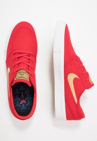 Czerwone płócienne trampki z białą gumową podeszwą. Posiadają złote logo Nike oraz teksturowaną czarno-niebieską wkładkę. Sznurówki pasują do koloru cholewki.