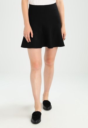 Jupe évasée noire en tissu doux et extensible, dotée d'une taille élastique et d'une texture lisse, associée à des chaussures noires à enfiler en matière pelucheuse.